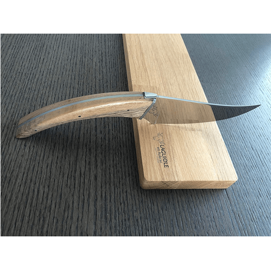 Cheese knife resting against an oak board on a dark wood surface