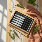 Boxed steak knife set on a table with rosemary, basil and a terracotta napkin