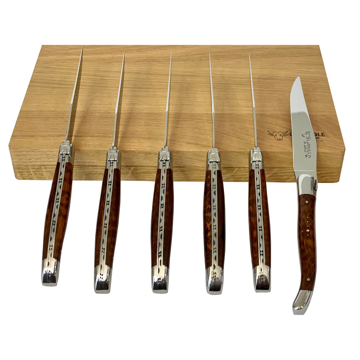 Six snakewood steak knives standing upright in front of the box