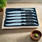 Boxed antler knives on a wooden table beside a small bowl with an olive