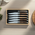 Boxed grapevine knives on a pale table with herbs and a wooden bowl