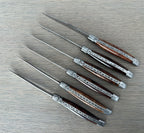 Six ironwood steak knives laid diagonally on a grey surface