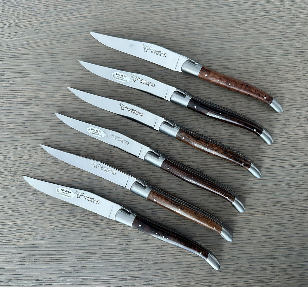 Six dark wood handled steak knives laid in a row