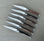 Six dark wood handled steak knives laid in a row