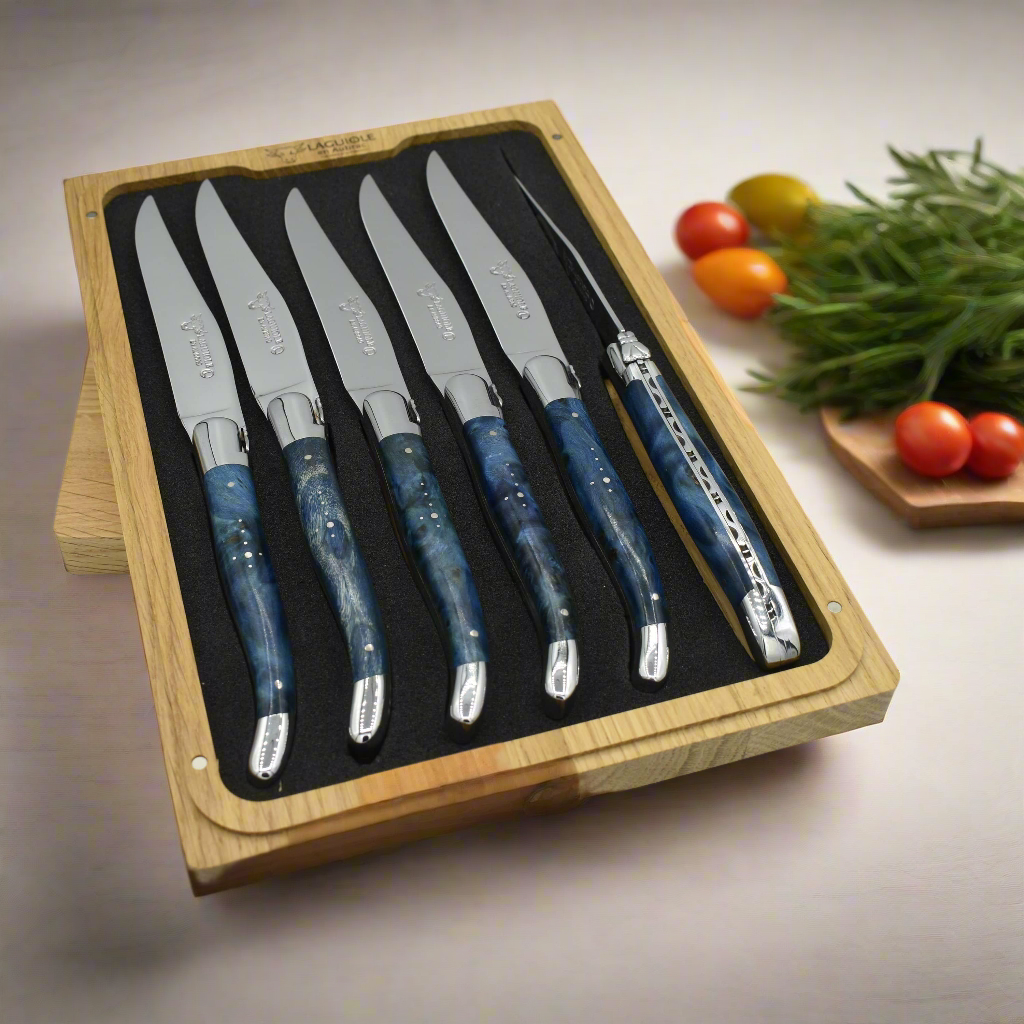 Boxed blue burl knives beside tomatoes and fresh herbs on a board