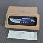 Violet handled corkscrew in an open oak box above the Laguiole en Aubrac certificate