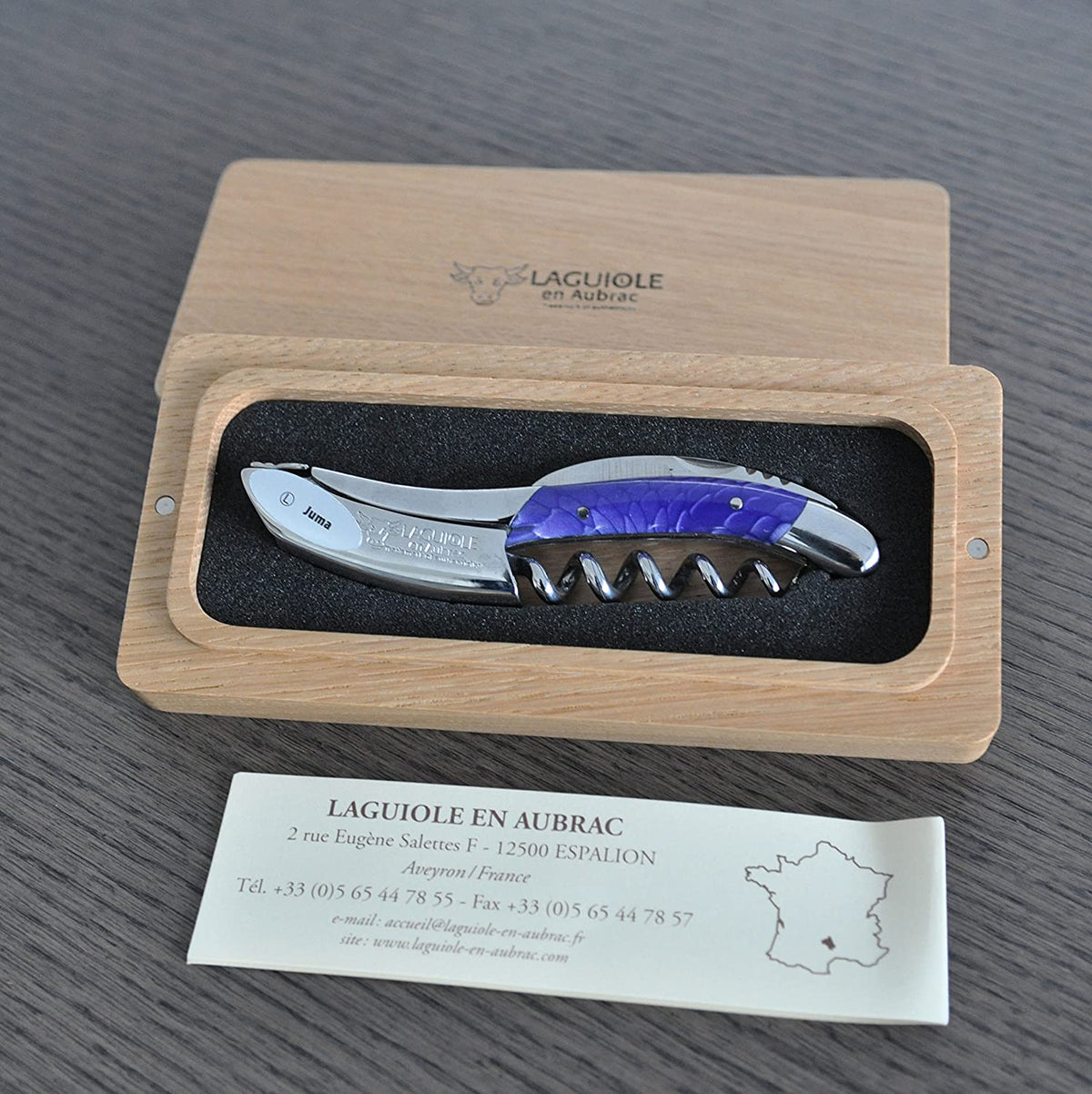 Violet handled corkscrew in an open oak box above the Laguiole en Aubrac certificate