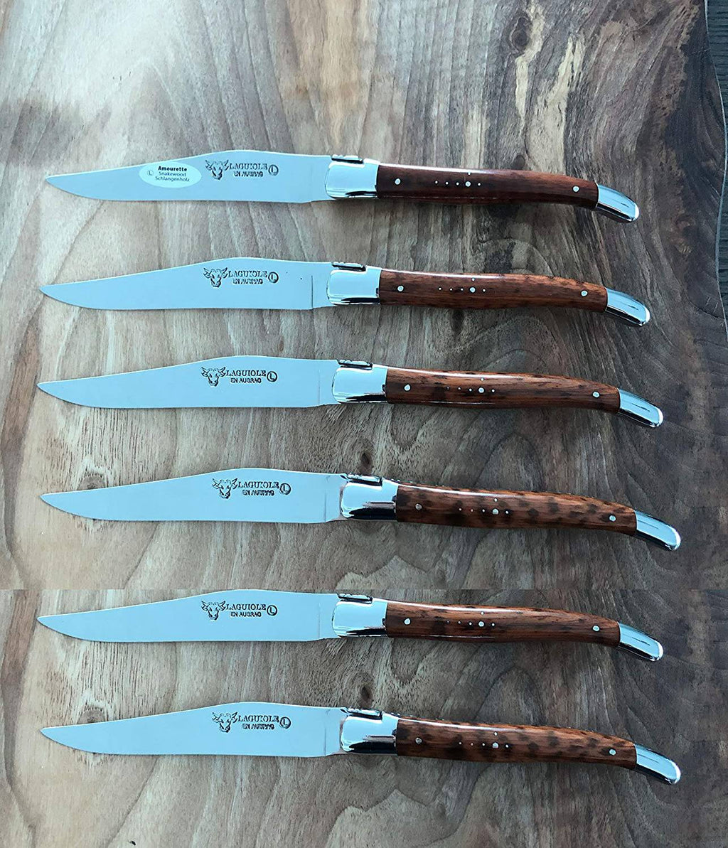 Six knives laid in a row on a dark stone surface