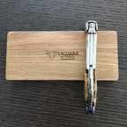 Folded corkscrew standing on edge against the engraved oak box