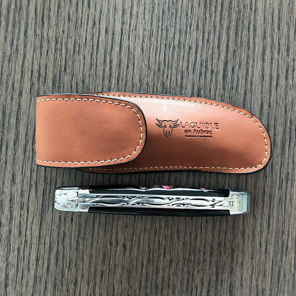 Brown sheath above a closed folding knife on a dark wood surface