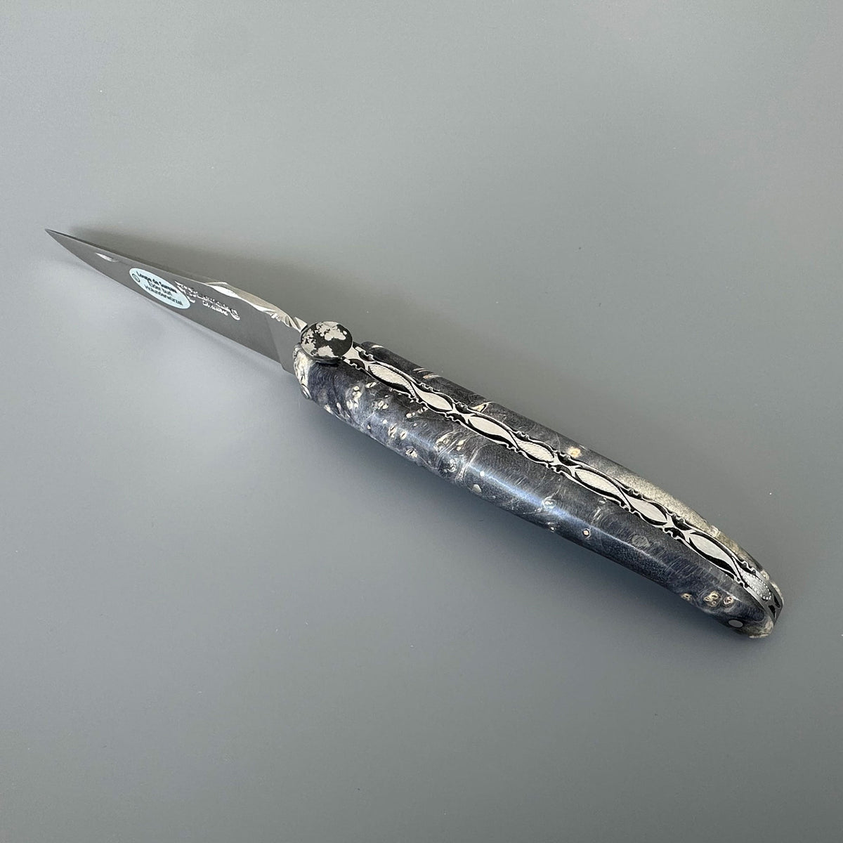 Laguiole Cosmos Earth dark knife with black and grey elder burl handle on grey