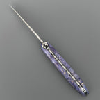 Laguiole Cosmos Earth purple knife with violet elder burl handle, open on grey
