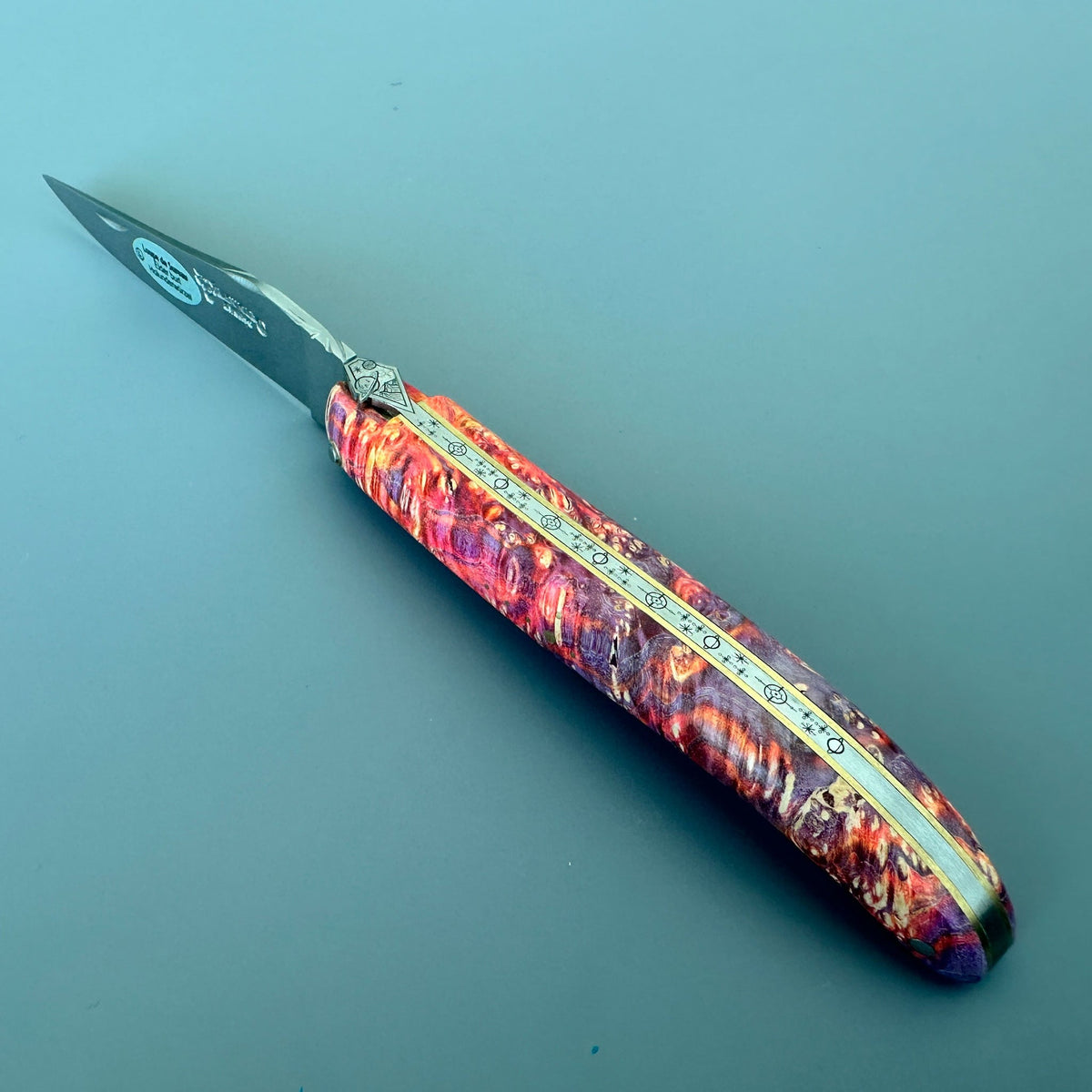Laguiole Cosmos Space Bee knife with bright fire elder burl handle on a blue background