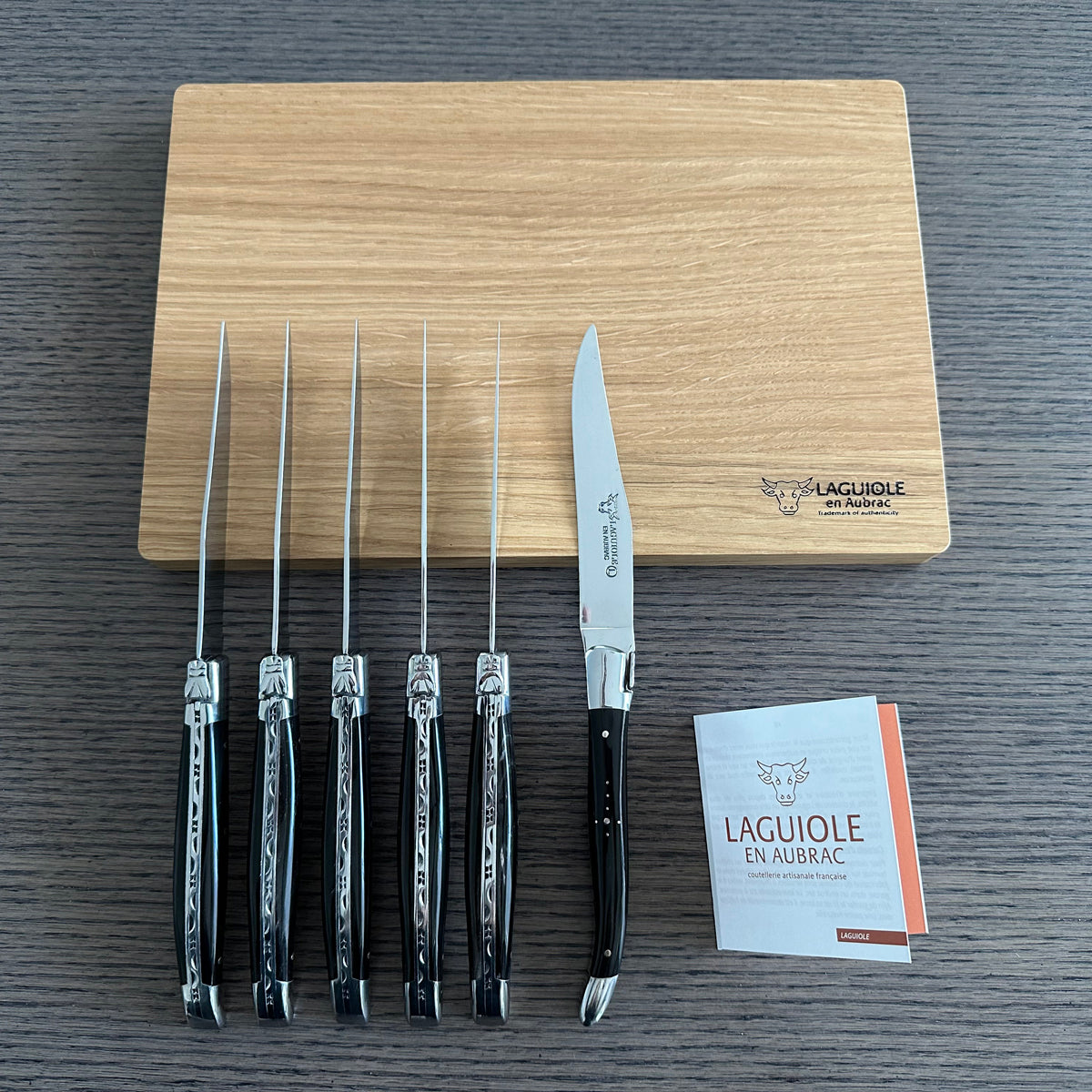 Six dark horn steak knives standing in a row beside their box and booklet