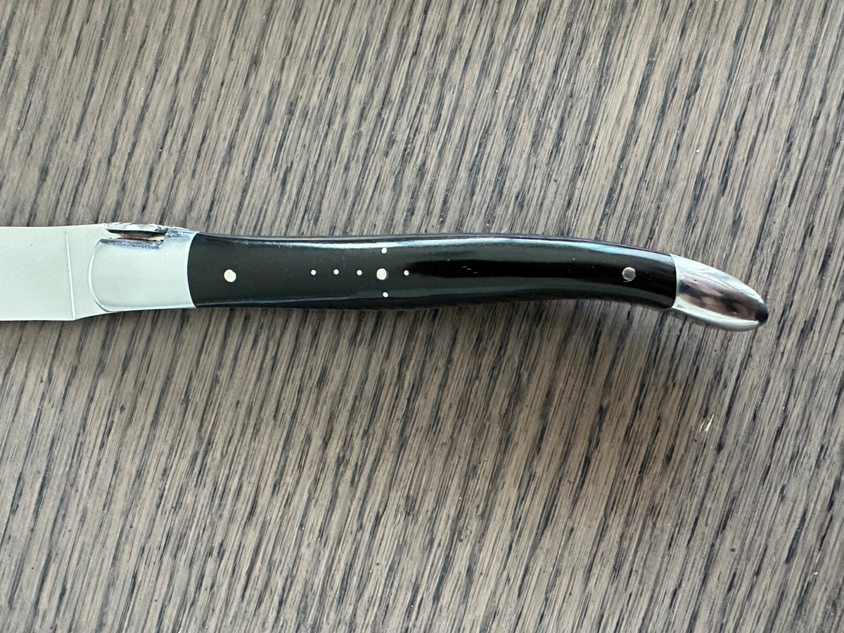 Close view of a black horn handle with steel pins and polished bolster