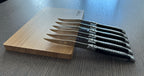 Six steak knives fanned along the edge of the wooden box