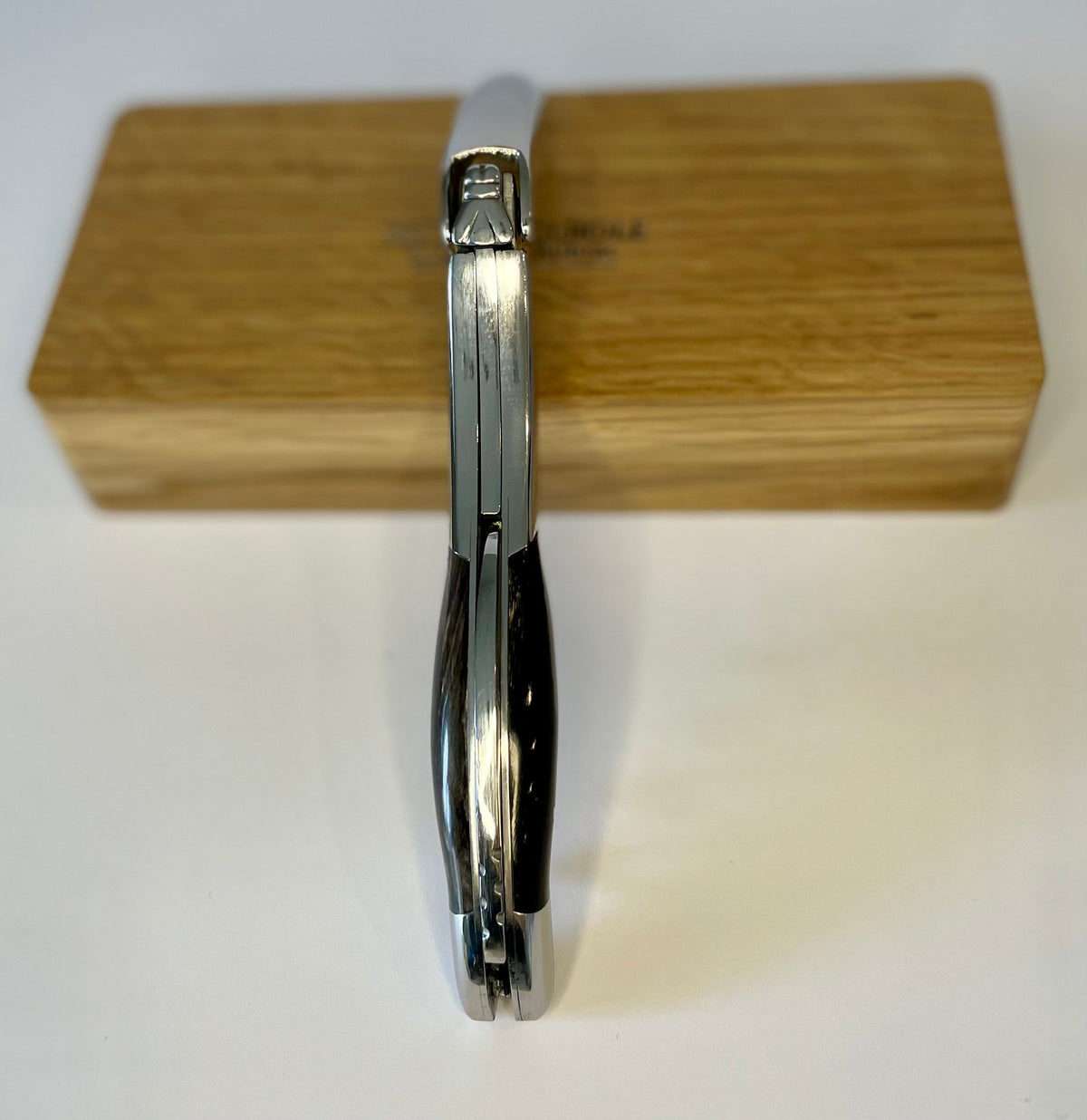 Folded corkscrew standing upright against the oak box, spine facing out
