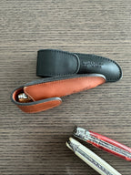 Black sheath and an open orange lined sheath beside two folding knives