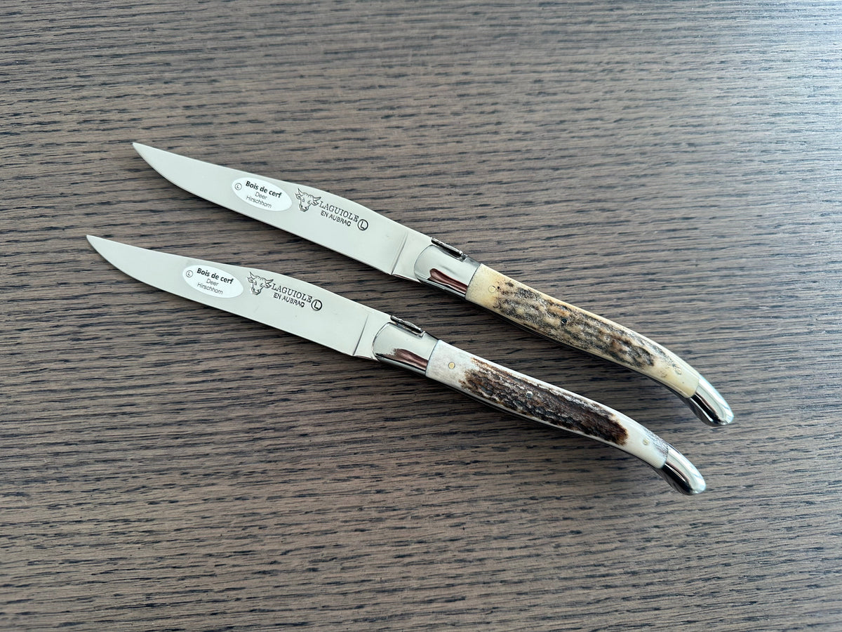 Two antler steak knives lying side by side on a dark table