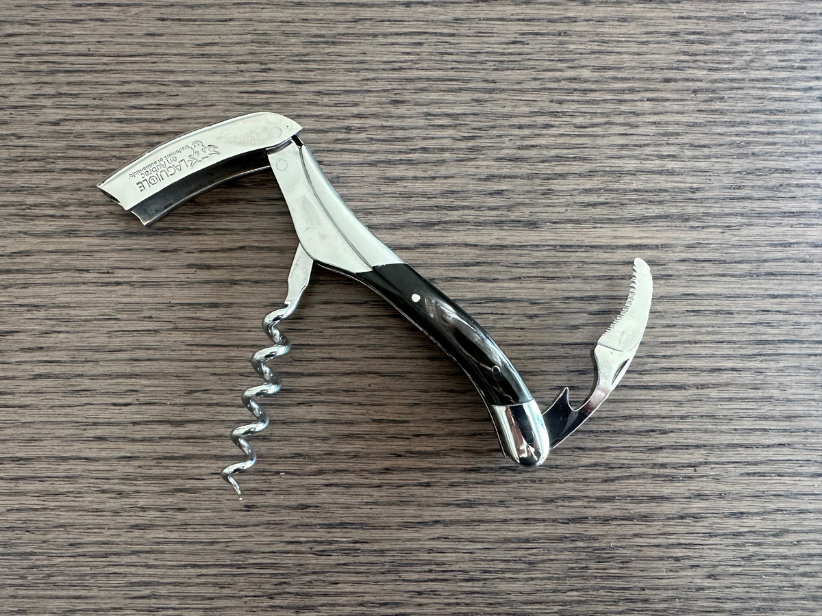 Opened corkscrew with the lever and spiral out on a wood table