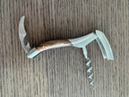 Opened corkscrew with the foil cutter and spiral out on a wood table