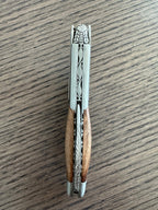 Folded corkscrew standing upright on a wood table, spine facing up