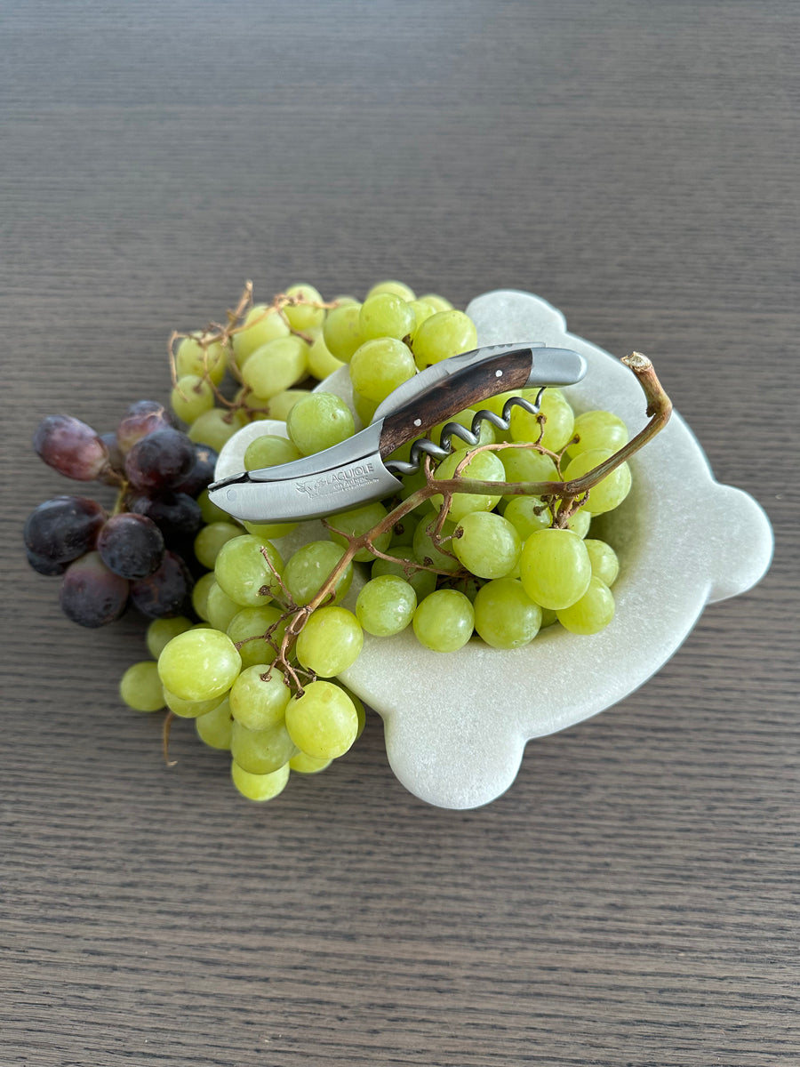 Corkscrew on a marble dish of green and red grapes