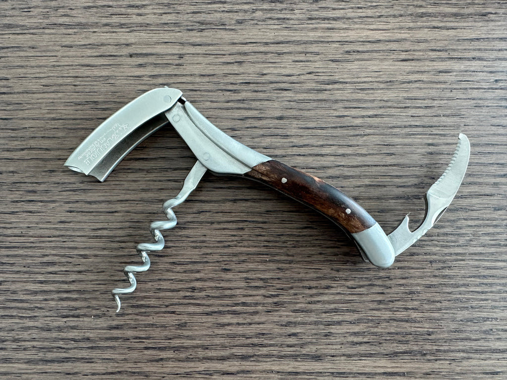 Opened corkscrew showing the foil cutter, spiral and lever on a wood table