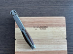 Folded corkscrew leaning on the engraved oak box, spine facing up