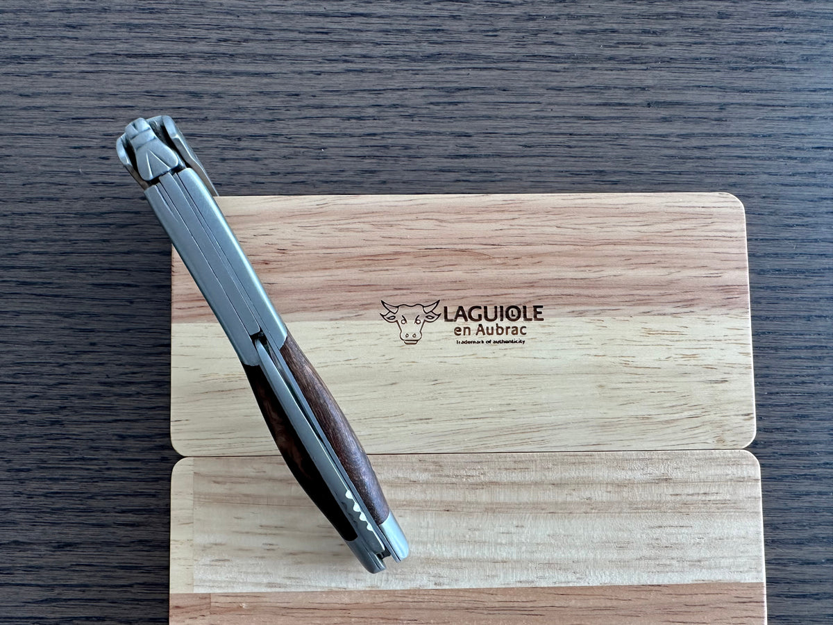 Folded corkscrew leaning on the engraved oak box, spine facing up