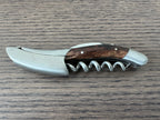 Folded grapevine wood corkscrew lying on a dark wood table