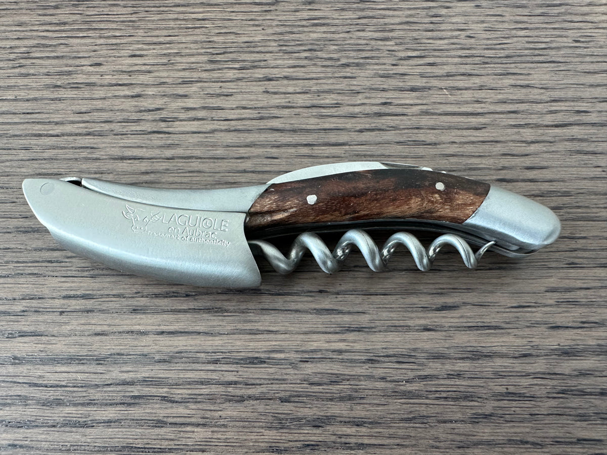 Folded grapevine wood corkscrew lying on a dark wood table