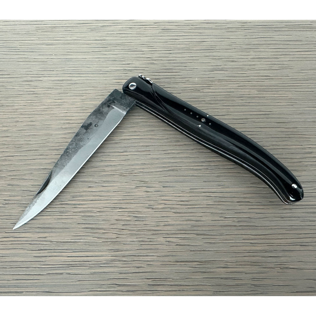 Half open rough forged knife on a pale wood surface