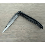 Half open rough forged knife on a pale wood surface