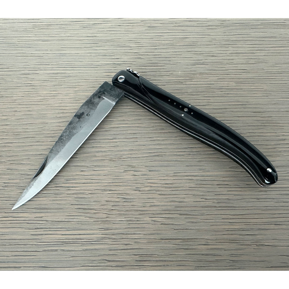 Half open rough forged knife on a pale wood surface