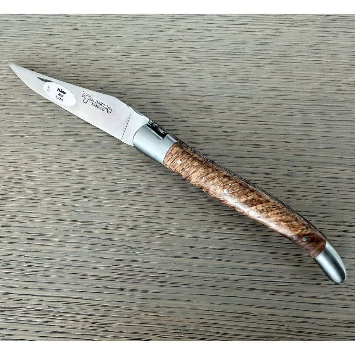 Open ash burl knife showing the engraved blade and bolster