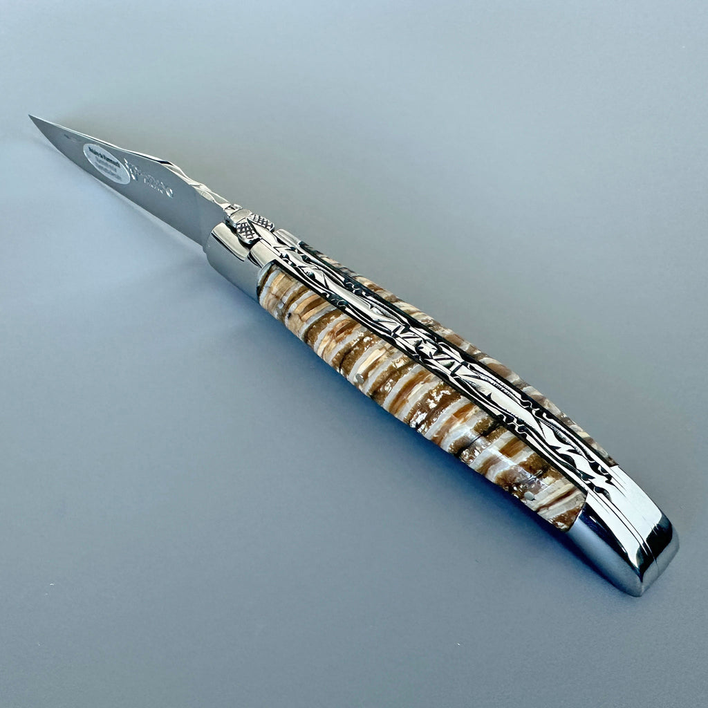 Laguiole mammoth molar knife with beige and brown banded handle on a blue grey surface
