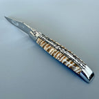 Laguiole mammoth molar knife with beige and brown banded handle on a blue grey surface