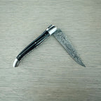 Laguiole Explosion Damascus buffalo horn knife half open on pale wood