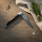 Half open knife on a dark wood table with peppercorns, herbs and linen