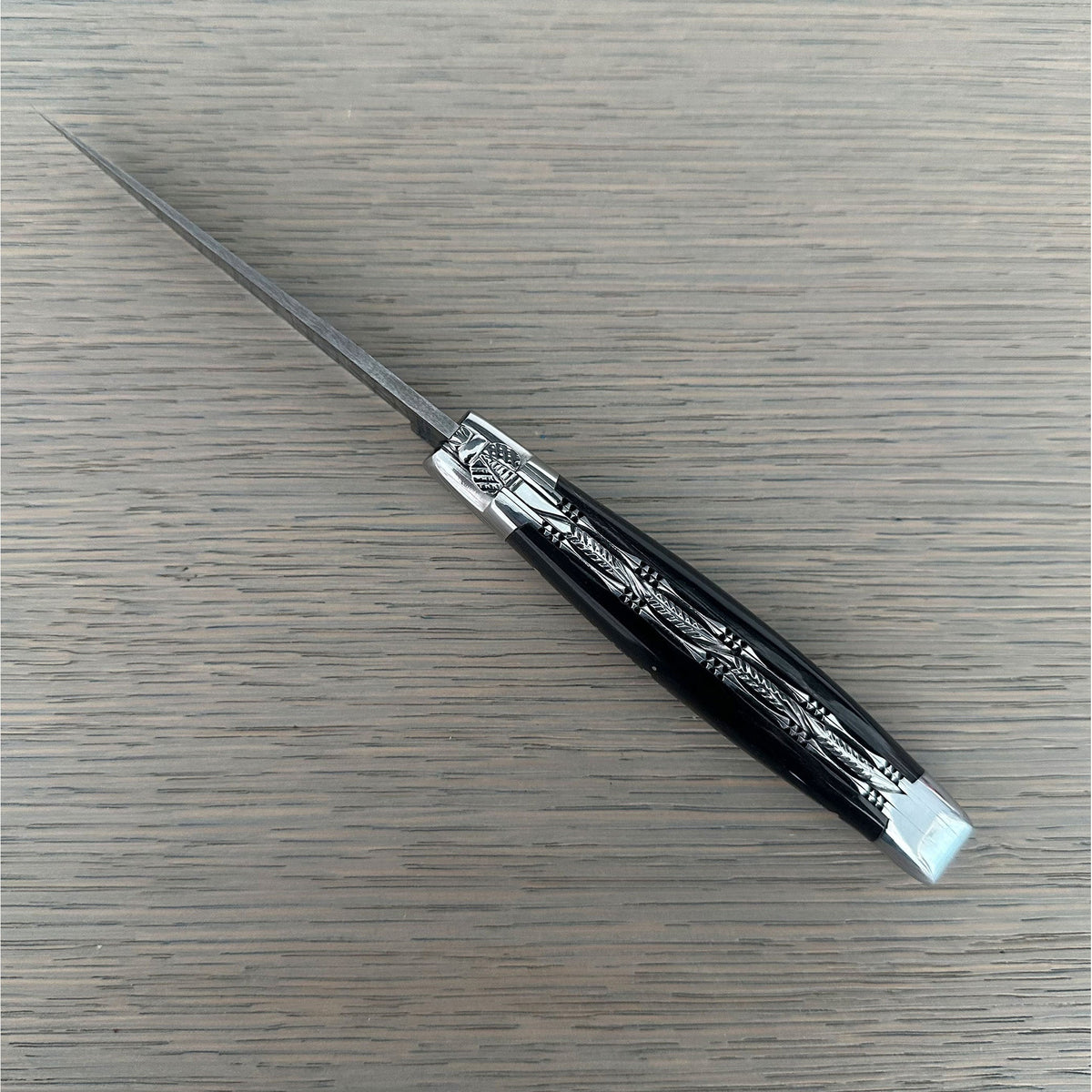 Open knife lying diagonally showing the black horn and filed plates