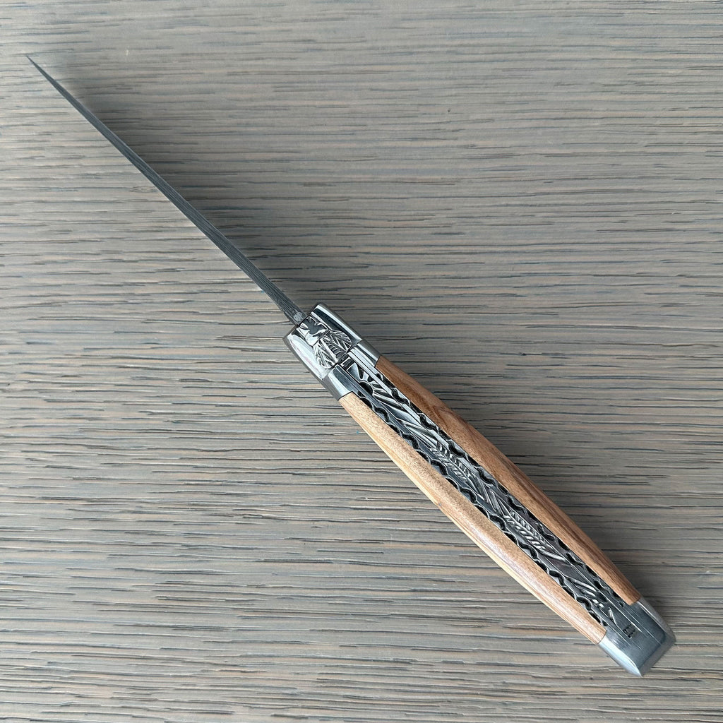 Open knife lying diagonally showing the olive wood and filed plates