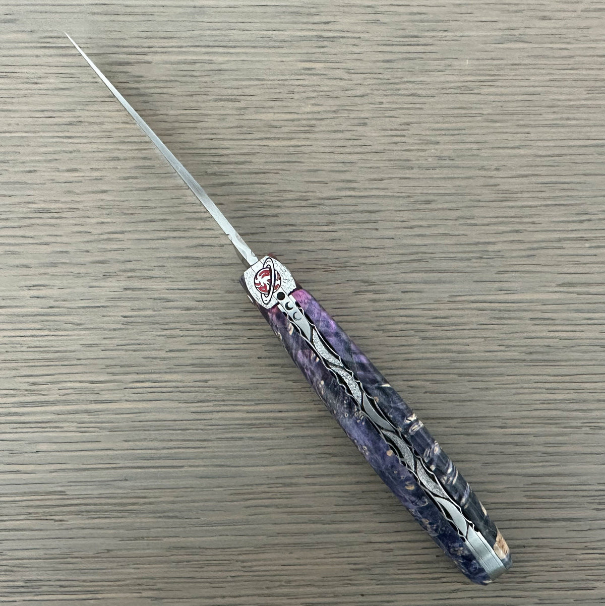 Laguiole Cosmos Saturn purple knife with indigo elder burl handle, open on pale wood