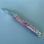 Laguiole Cosmos Saturn fire knife with red and pink elder burl handle on a blue background