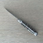 Open knife lying diagonally on pale wood