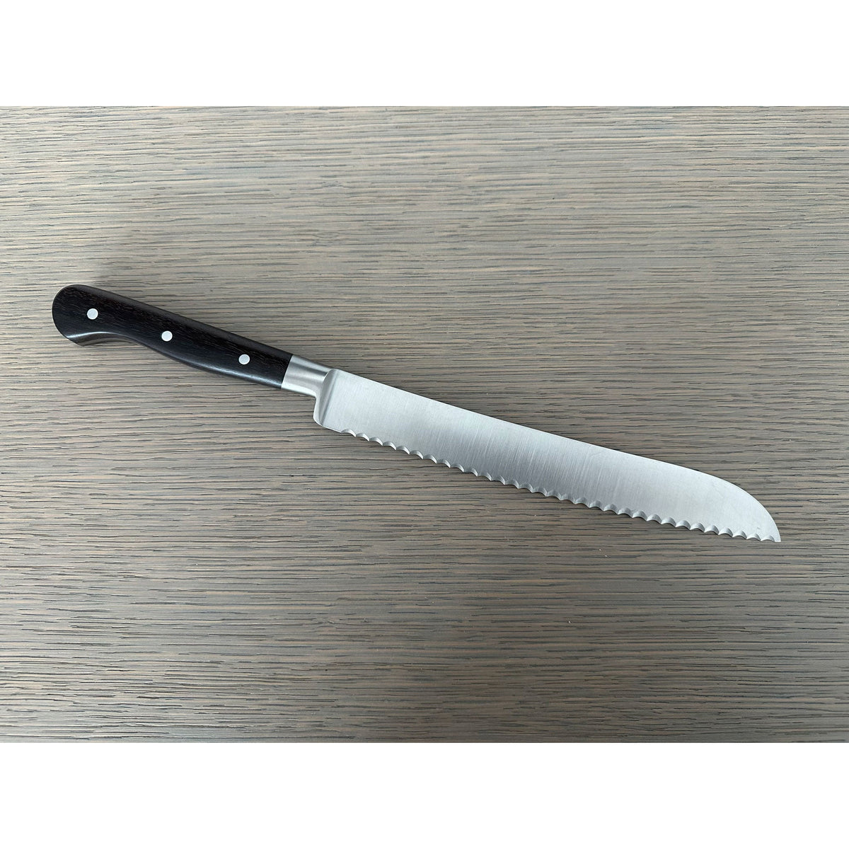 Bread knife lying with the serrated blade pointing down and right
