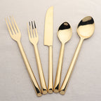 Set of gold cutlery including forks, knives, and spoons on a light gray background