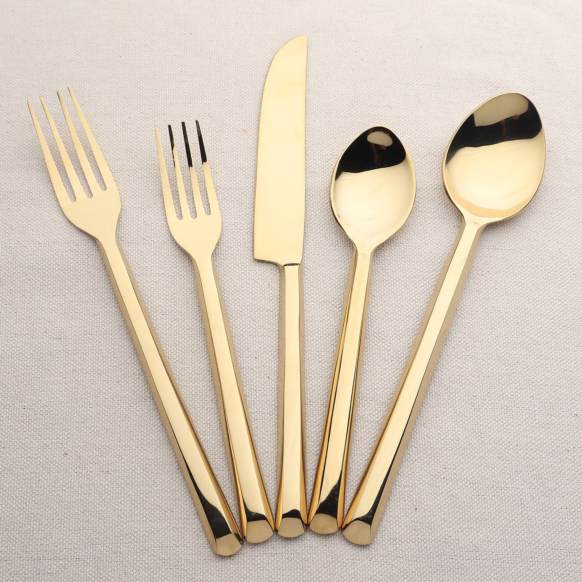 Set of gold cutlery including forks, knives, and spoons on a light gray background