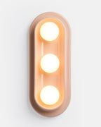 triple globe ceramic sconce in Pink Glossy beside a sofa