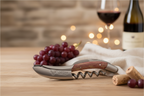 Corkscrew on a wooden table with red grapes, corks, a wine glass and a bottle